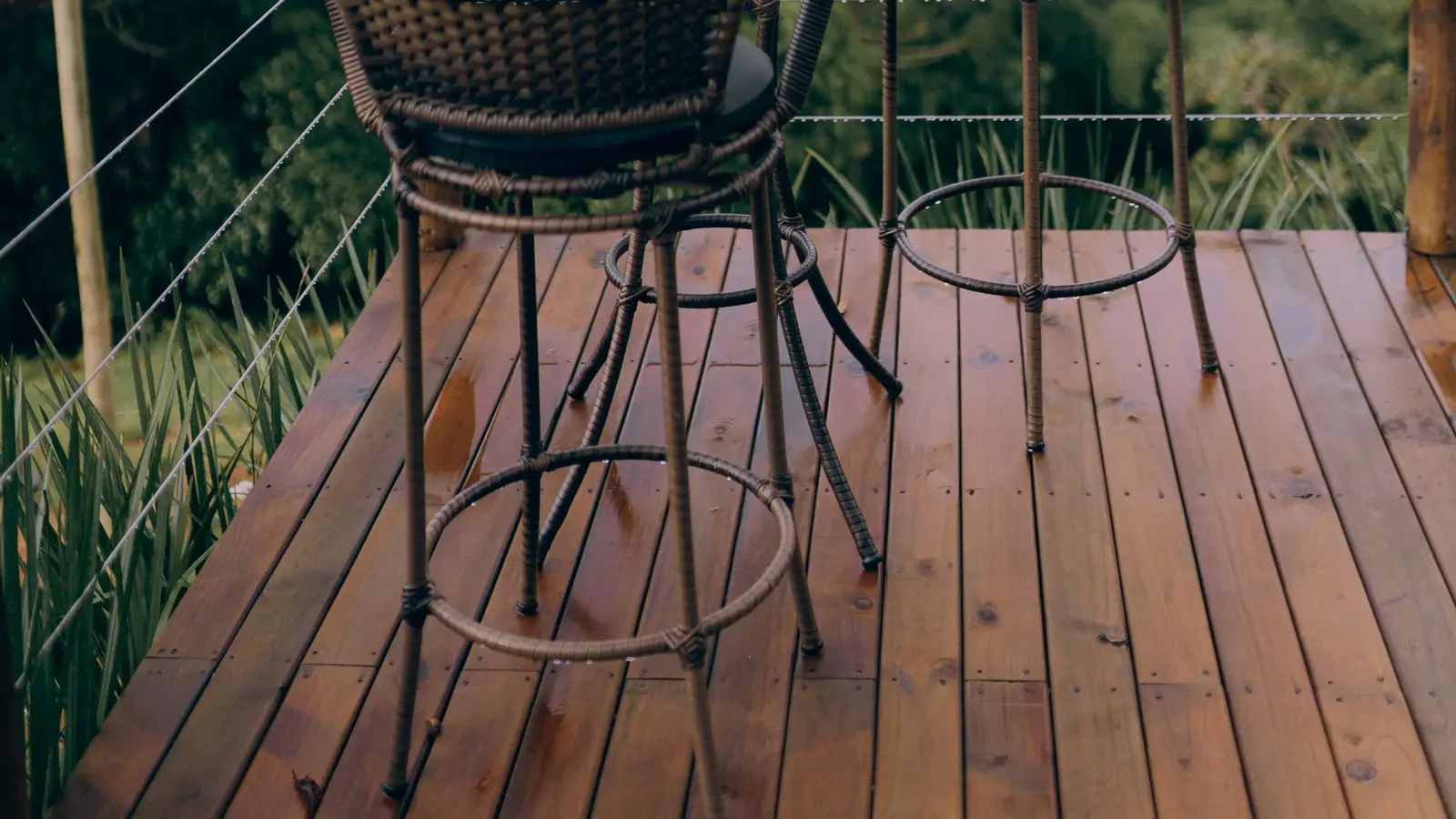 Cable railing on a deck with a bistro table and chairs above a wooded valley