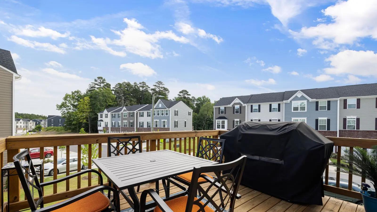 Wood deck with a dining table, chairs and a covered grill above a suburban street