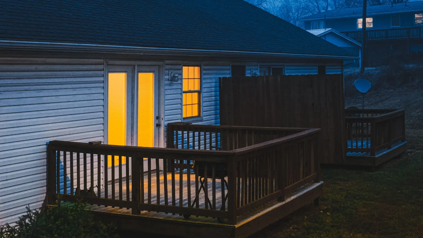 Back of a house at dusk with lit windows and a raised deck