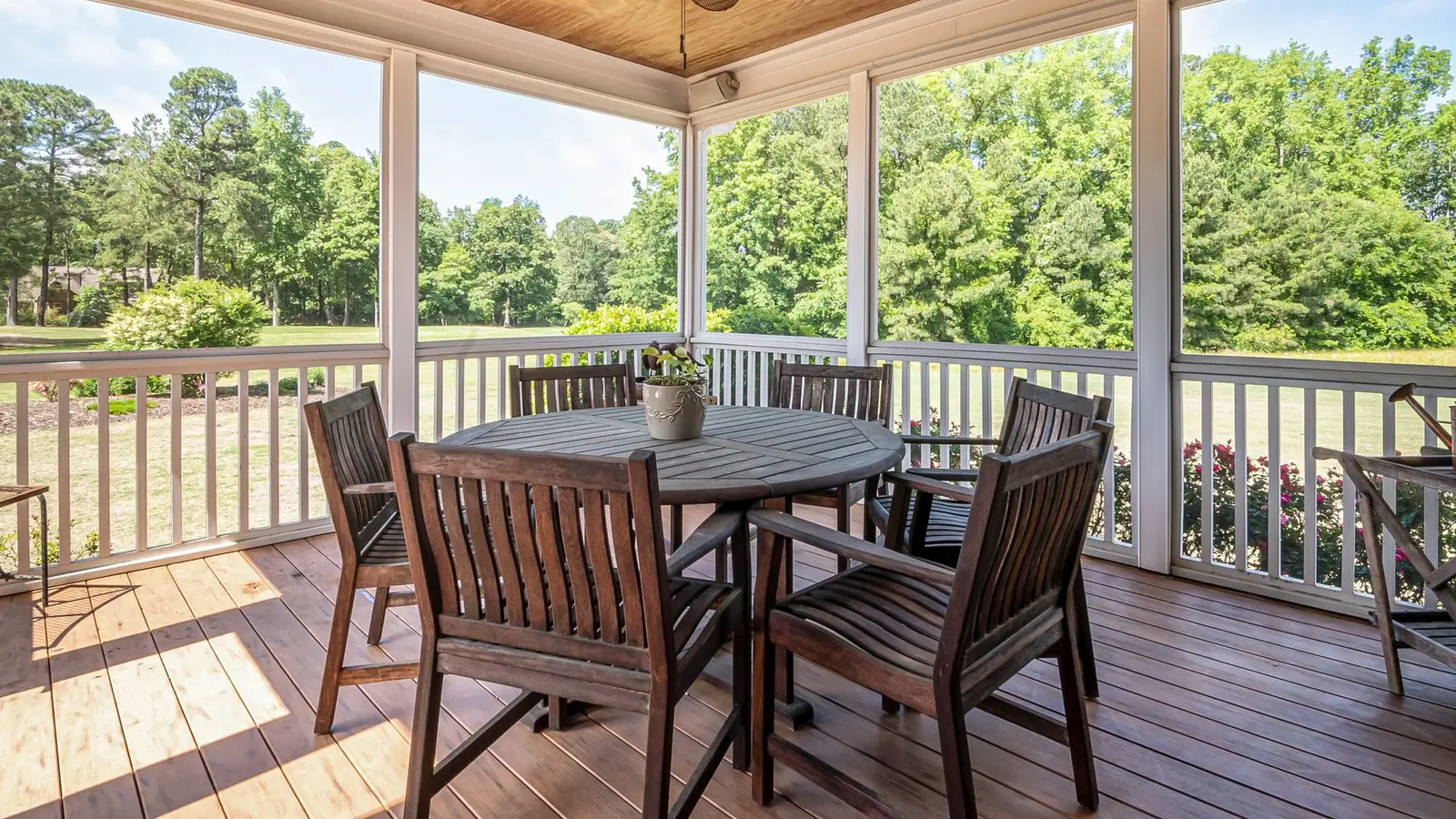 Screened porch with a wood dining set looking over a green lawn