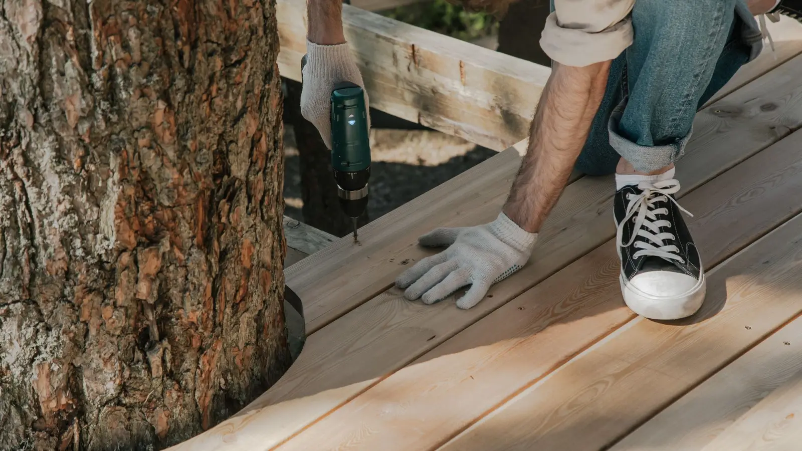 Worker in gloves driving screws into new wood deck boards
